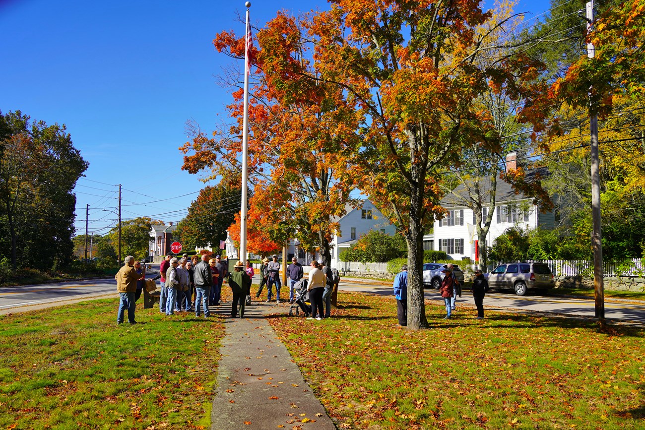 Group of people standing underneath tree with orange and red leaves