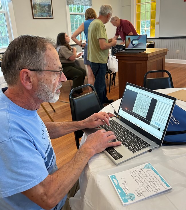 Man sits at desk with computer and pad of paper