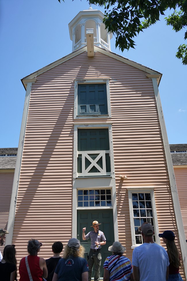 Park Ranger stands in front of Old Slater Mill belltower in front of group of visitors