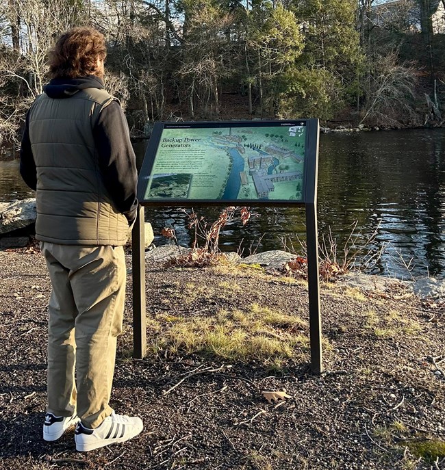 Man standing reading wayside exhibit by water