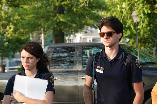 Young man and young woman stand next to each other listening to presenter