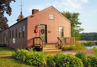 Wooden building painted red with cupola on the roof. Plants in the foreground