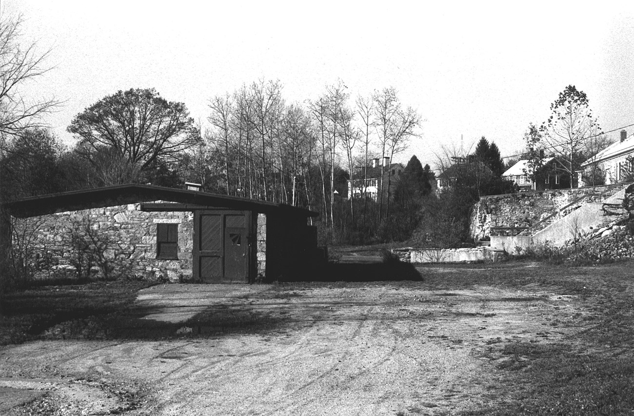 Image with stone mill building in foreground and hill with brick buildings on top of hill in the background