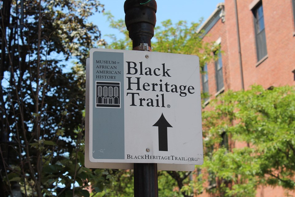Photograph of a cast iron gas lamp with a steel street sign with the words "Black Heritage Trail" and an arrow pointing ahead.