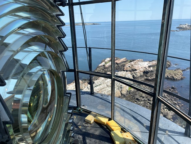 Close view of the lighthouse's fresnel lens, with the view of the ocean in the background
