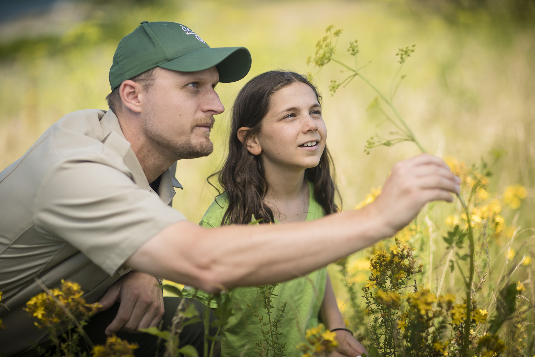 DCR ranger kneeling next to girl, both looking at flowers