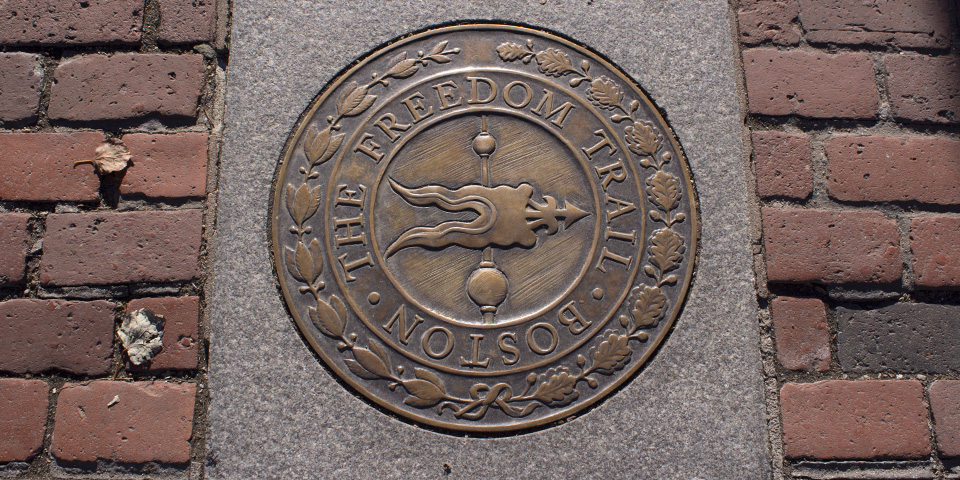 Bronze sidewalk marker medallion with words The Freedom Trail Boston. Weathervane bas relief is in center.