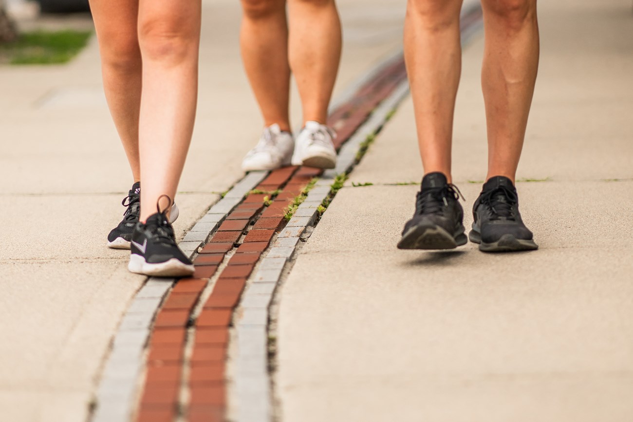 People walking along a red brick line in the sidewalk.