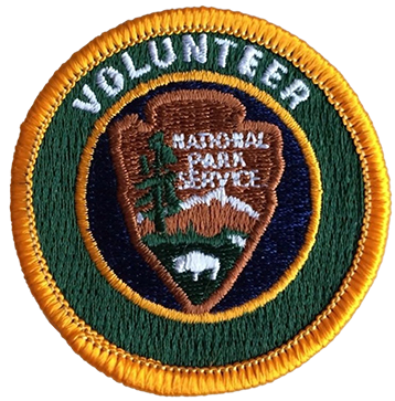 A volunteer patch of the National Park Service with an arrowhead and a bison, mountain, and tree.