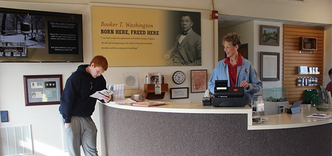 A female volunteer at the visitor center and a visitor reading information.