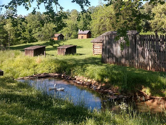 A photograph of a grouping of rustic farm structures and a rustic cabin in the background.