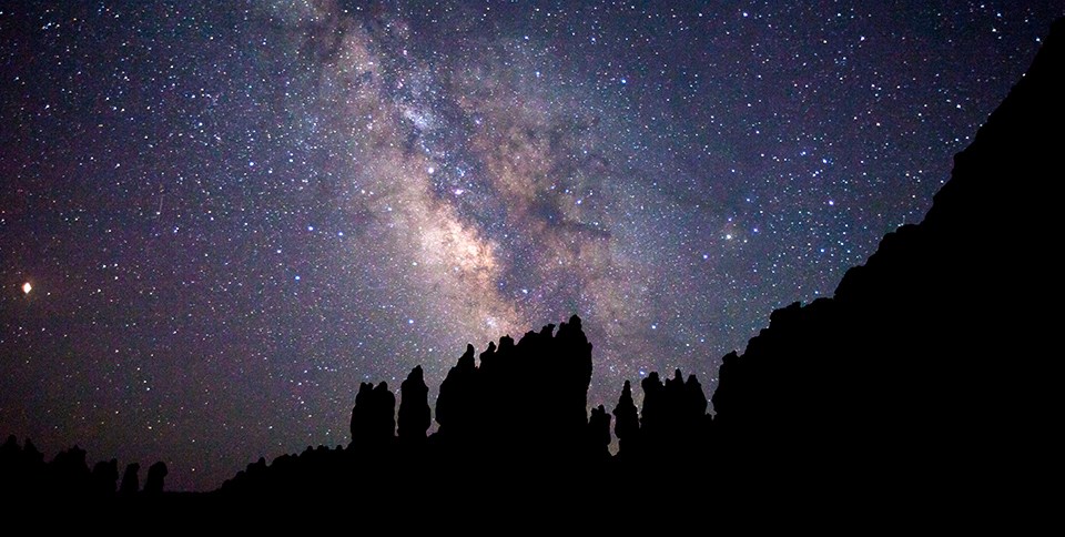 Milky way galaxy and a sky of stars above a silhouette of rock spires and cliffs