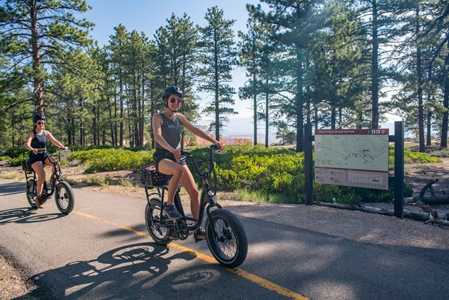 Two people riding electric bikes on a black asphalt path.