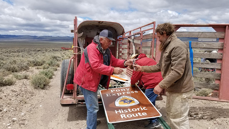 People help each other get a large brown sign out of the back of a truck.