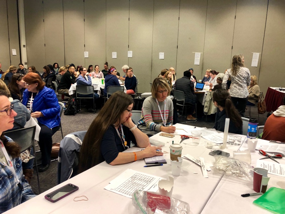  Conference attendees gather around tables filled with various plastic objects for a workshop on the Marine Impacts of Plastic Use and Disposal.