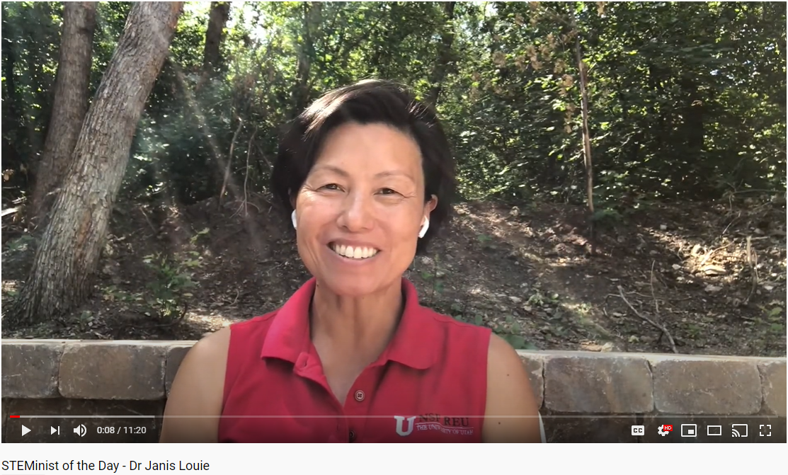 A screenshot of a smiling Asian woman in a red University of Utah shirt with a stone wall and trees behind her.