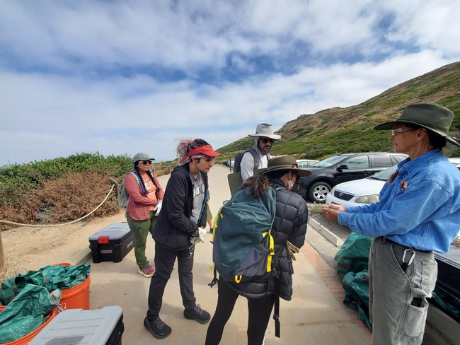 A park staff member, who is holding non-native plant specimens in her hand, stands in front of a volunteer group.