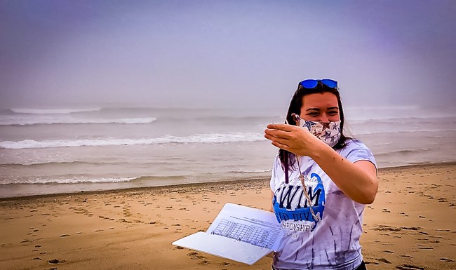 Volunteer stands on beach holding a clipboard of sample data.