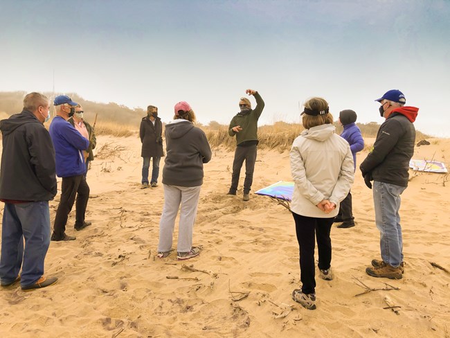 Several volunteers stand on a beach as they gather around an instructor.