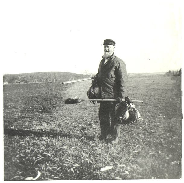 A man stands in a grassy field in a black and white photograph from the 1800s.