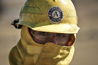 A person wearing a yellow face mask, yellow hard hat, and safety glasses.