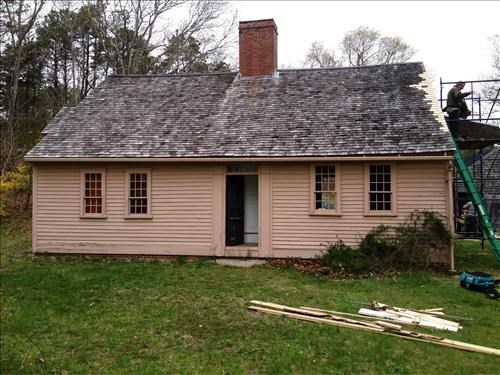 Brown cape cod style home with roofing materials in image.
