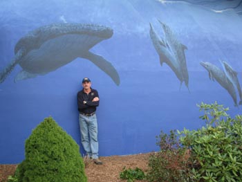Large mural with blue water and black and white whales. Man stands in front of it.