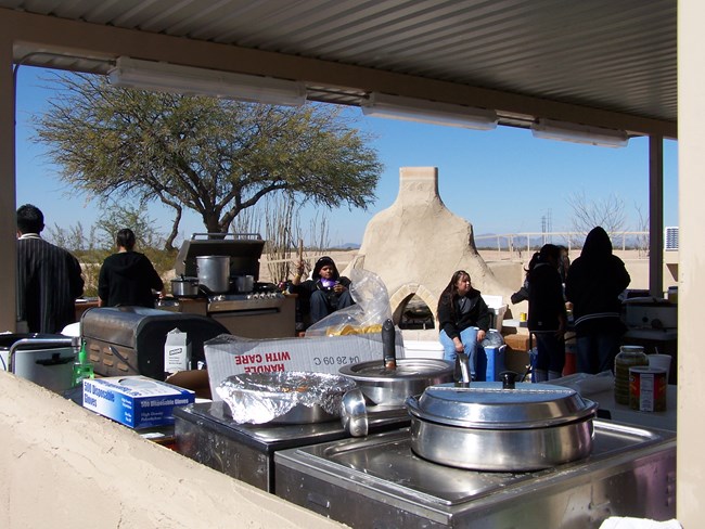 outdoor kitchen in use showing pots on stove and people in background