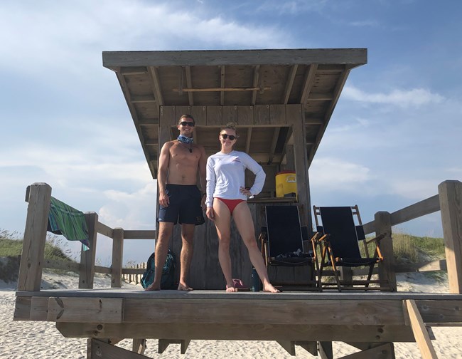 Two lifeguards stand on deck of lifeguard shack on the beach.
