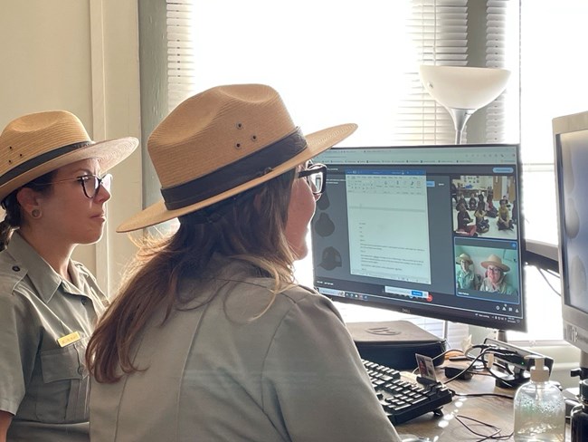Two rangers sit at computer screens giving virtual program.