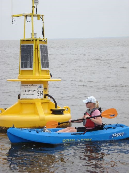 A kayaker paddles in front of a NOAA buoy