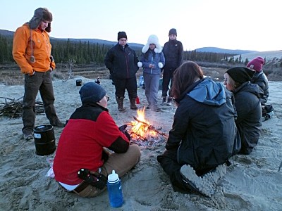 campers in warm clothes stand around a campfire