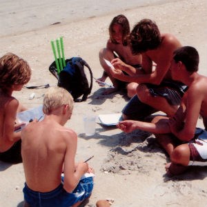 Boys work on their Junior Ranger Adventure booklets in the sand.