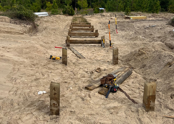 Construction of boardwalk on sand leading into pine trees