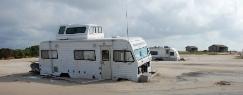 An RV buried to its wheels in sand after a hurricane.