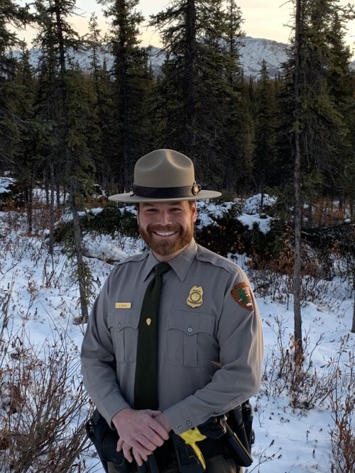 Chief Ranger Nick Pulfer smiles at the camera, with trees behind him.