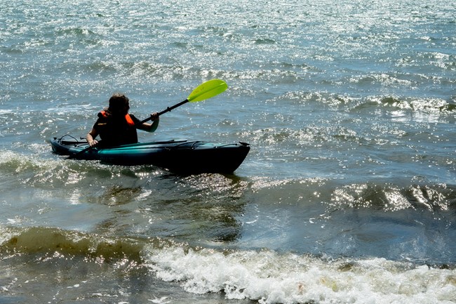 a kayaker wearing a personal flotation device paddles in thew water