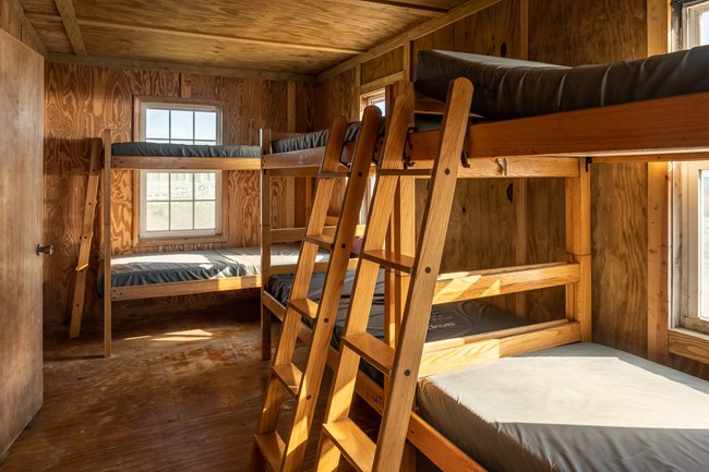 Three bunk beds with a window in the background. The sun fills the room, leaving streaks on the beds and walls.