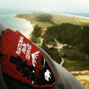 The National Patch Service patch on a ranger's shirtsleeve with the view from the top of the lighthouse in the background.