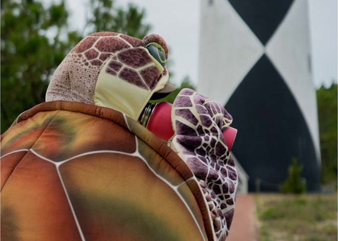 a person in a sea turtle costume drinking a water bottle with lighthouse in the background