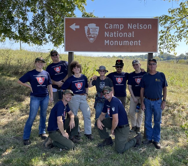 NPS staff and volunteer post for an image by a brown NPS sign.