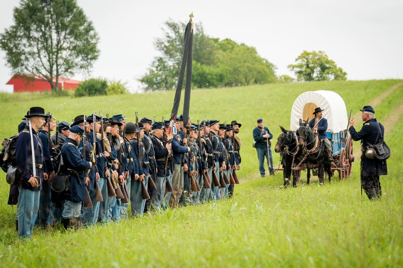 Living history interpreters in US Army uniform in line with mule-drawn wagon.