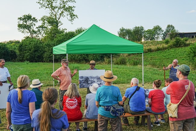 A Park Ranger talking to a group of visitors in a grass field.