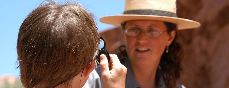 a student looks at a ranger through a magnifying lens