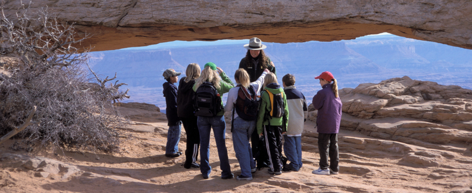 a group of children and a ranger stand at a broad stone arch