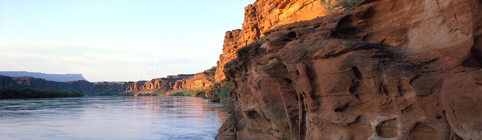 A calm river flows past orange cliffs