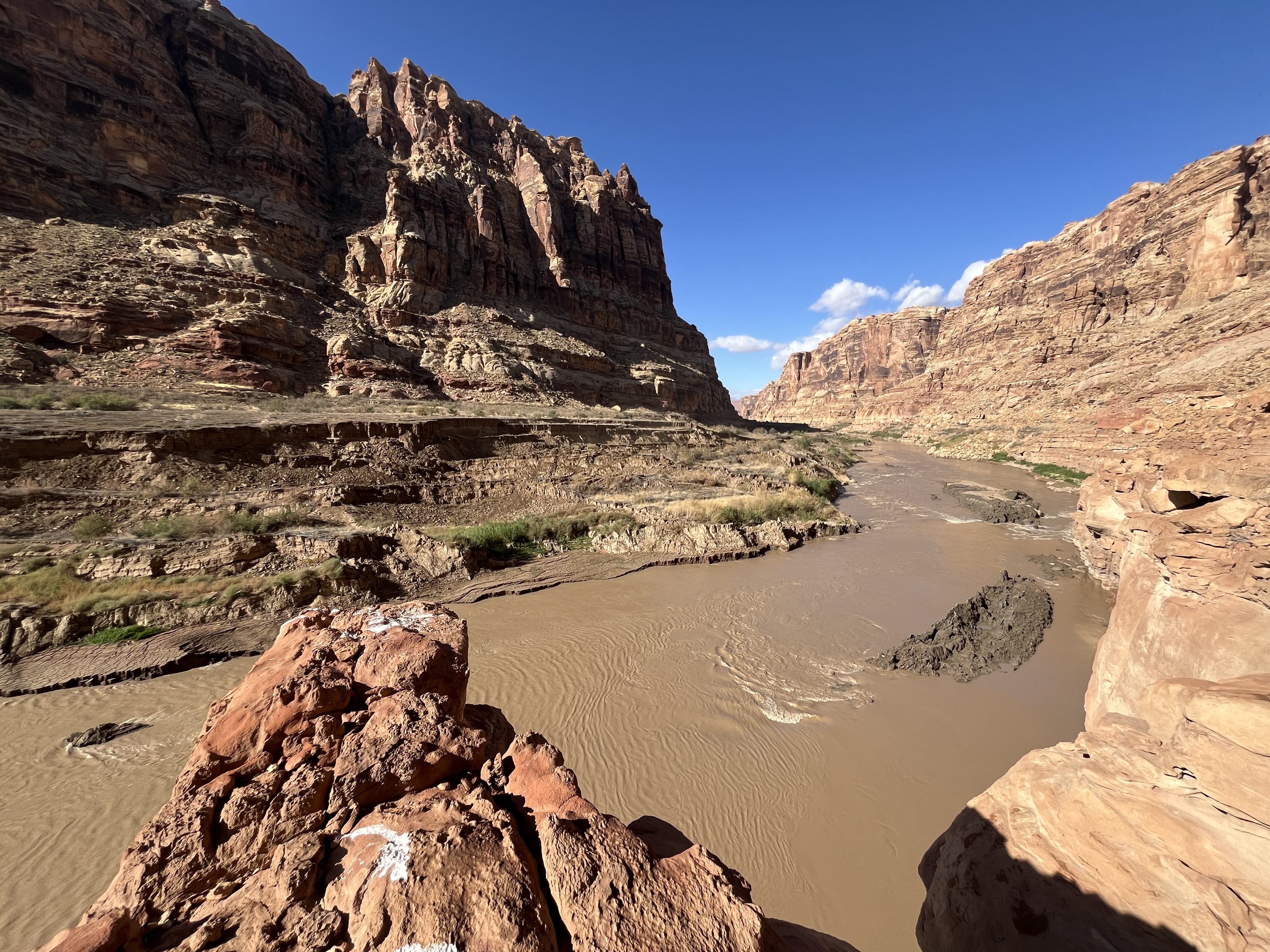 flowing brown water and mud at bottom of rocky river canyon, blue sky above