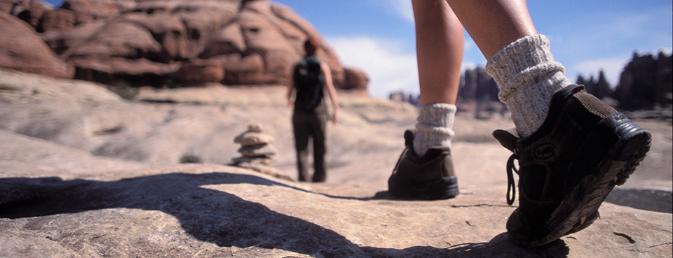 Two hikers walk away from the camera on a slickrock surface