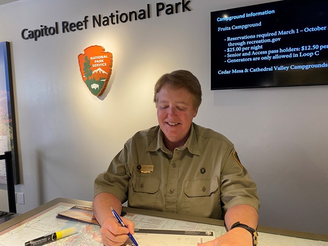 A volunteer assists an unseen visitor at the visitor center desk.