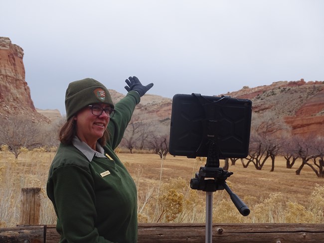 A ranger stands in front of an iPad, pointing at the cliffs in the background